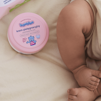 Różowy krem Bambino pielęgnacyjny dla noworodków, 200 ml, obok jasnej nóżki dziecka na beżowym kocu.