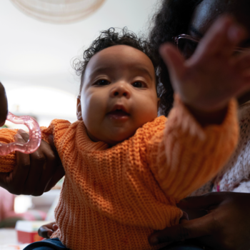 Niemowlę w pomarańczowym sweterku z gryzakiem, bliskie ujęcie, obrazujące produkt BoboVita dla dzieci.