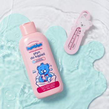 Bambino Płyn do Kąpieli dla niemowląt, różowa butelka z misiem, obok termometr, widok z góry na wodnym tle.