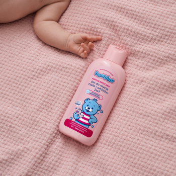 Różowa butelka Bambino Żel 2w1 dla niemowląt z misiem, leży na różowym kocu obok ręki dziecka.