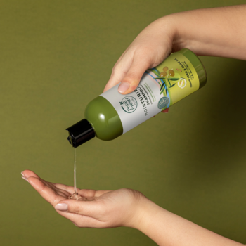Ręce wylewają szampon nawilżający Petal Fresh Pure z oliwy i winogron z zielonej butelki do dłoni.