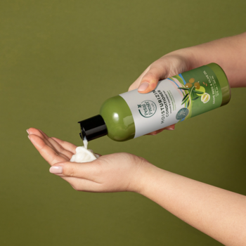 Dłonie wylewają kremową odżywkę Petal Fresh Pure z winogron i oliwek z zielonej butelki z pompką na dłoń.