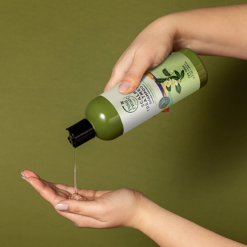 Szampon Petal Fresh Pure z olejkiem herbacianym w oliwkowej butelce, wylewany do dłoni na zielonym tle.