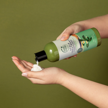 Osoba wylewa Petal Fresh Pure odżywkę do skóry głowy z drzewa herbacianego z zielonej butelki do dłoni.