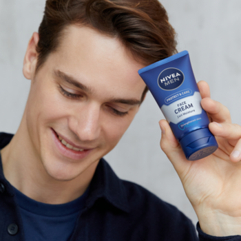 Uśmiechnięty mężczyzna w niebieskiej koszuli trzyma niebieski krem do twarzy NIVEA MEN Protect & Care.