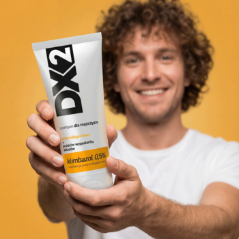 Uśmiechnięty mężczyzna trzyma białą tubę szamponu DX2, przeciwłupieżowego i na wypadanie włosów, na pomarańczowym tle.