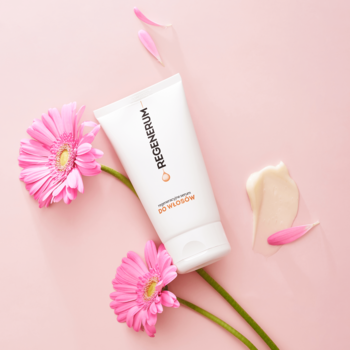 Biała tuba Regenerum regeneracyjne serum do włosów na różowym tle, obok różowe gerbery i kremowy swatch.
