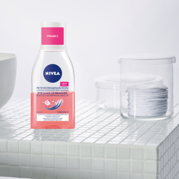 NIVEA Dwufazowy płyn do demakijażu oczu z Witaminą C, butelka z różową warstwą na białych płytkach.
