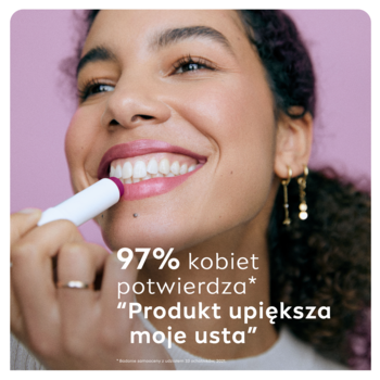 Uśmiechnięta kobieta aplikuje koloryzującą pomadkę NIVEA jeżynową. Biały sztyft z fioletowym odcieniem.