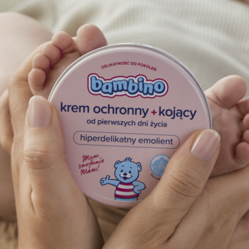 Różowy słoiczek kremu Bambino ochronny+kojący od pierwszych dni życia, trzymany w dłoniach, stopy w tle.