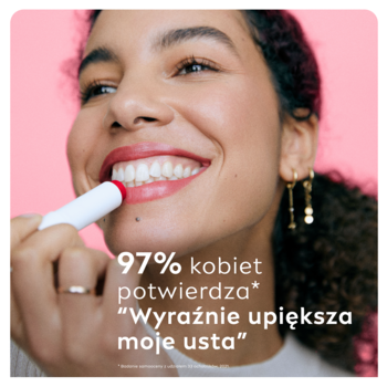 Uśmiechnięta kobieta nakłada truskawkową pomadkę koloryzującą NIVEA, biały sztyft. Różowe tło.