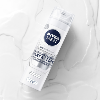Regenerująca pianka do golenia NIVEA MEN Sensitive, biała butelka, widok z góry na tle z mlecznymi smugami.