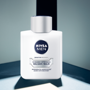 Frontowy widok białego NIVEA MEN Sensitive Regenerujący Balsam po goleniu ze srebrną zakrętką, na tle geometrycznym.