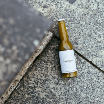 Mętna lemoniada Matcha w smukłej butelce na tle szarego, kamiennego podłoża, widok z góry, etykieta MATCHATA.