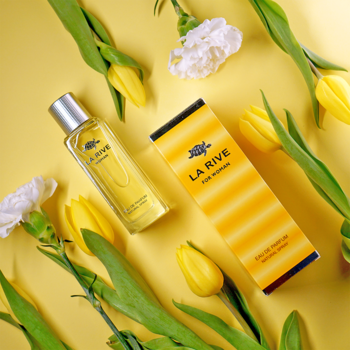 Żółte perfumy LA RIVE FOR WOMEN EDP w butelce i kartoniku, widok z góry, ułożone pośród żółtych tulipanów i białych kwiatów na żółtym tle.