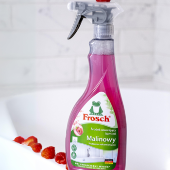 Różowy odkamieniacz Frosch Malinowy w butelce spray, widoczny w białej wannie z malinami.