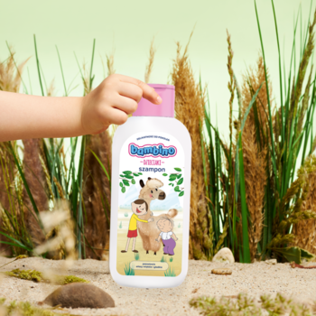 Dziecko trzyma biały szampon Bambino Alpaka 400 ml z różową nakrętką na tle traw i piasku.