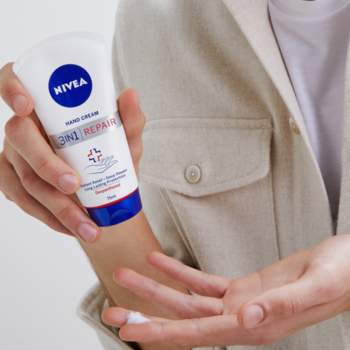 Krem Nivea 3w1 Repair w białej tubce z niebieską nakrętką, osoba nakłada produkt na dłoń.