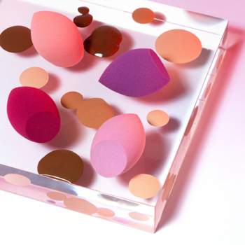 Minigąbki Miracle Complexion Mini Sponges: różowe, fioletowe, pomarańczowe, na akrylowej tacy z podkładem.