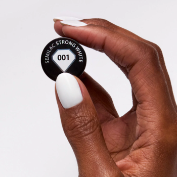 Zbliżenie dłoni trzymającej czarny korek lakieru hybrydowego Semilac 001 Strong White. Biały paznokieć.