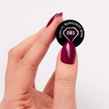 Dłoń trzyma czarny, okrągły wzornik Semilac 083 Burgundy Wine, głęboki fiolet z wiśniowym odcieniem. Pomalowane paznokcie.