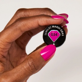 Ciemna dłoń z neonową fuksją na paznokciach trzyma nakrętkę lakieru Semilac 034 Mardi Gras.