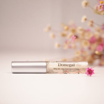 Zbliżenie: Donegal transparentny klej do rzęs z pędzelkiem, tubka ze srebrną nakrętką, obok różowy kwiatek.