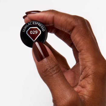 Ciemna dłoń trzyma czarny korek Semilac Espresso 029. Na paznokciu błyszczący, ciemnobrązowy lakier do paznokci.