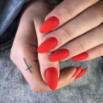 Dłonie z długimi, czerwonymi paznokciami o matowym, zamszowym wykończeniu Semilac Top Mat Total. Widoczny tatuaż.