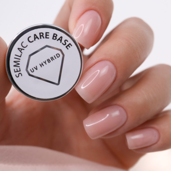 Ręka z delikatnymi, różowymi paznokciami trzyma okrągłą bazę Semilac Care Base UV Hybrid, białe wieczko z logo.