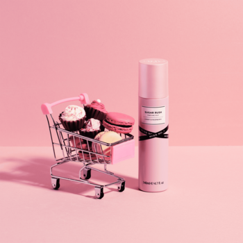 Różowa mgiełka perfumowana Miss So...? Sugar Rush, obok miniaturowego wózka z babeczkami i makaronikami.