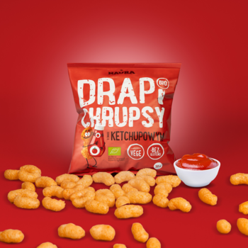 Czerwona paczka Drap Chrupsy Ketchup na jasnoczerwonym tle, obok rozsypane chrupki kukurydziane i miseczka ketchupu.