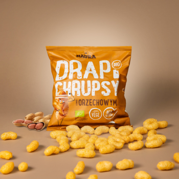 Pomarańczowa paczka DRAP CHRUPSY orzechowe BIO, z rozsypanymi puszystymi chrupkami i orzeszkami. Front.