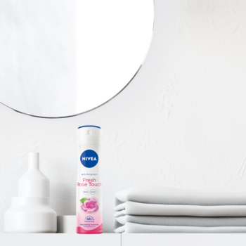 NIVEA Fresh Rose Touch antyperspirant w sprayu, biało-niebieska butelka z różą, na białej półce łazienkowej.