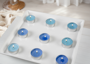 Zestaw dziewięciu zapalonych świec zapachowych antytabak w błękitnych woskach, na białej tacy.