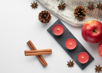 Widok z góry na trzy czerwone świece Jabłko-Cynamon w czarnej tacy. Wokół jabłka, cynamon, anyż.