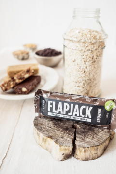 Ekologiczny baton owsiany kakaowy Flapjack Brownie na drewnie, słoik z owsem z tyłu.