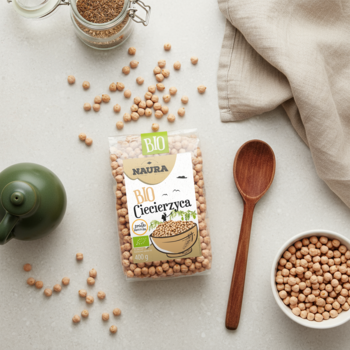 Płaskie ujęcie opakowania bio ciecierzycy Naura, rozsypane ziarna, miska, drewniana łyżka na jasnym tle.