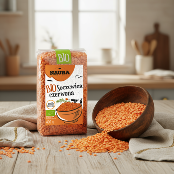 Naura BIO Czerwona Soczewica w opakowaniu i rozsypane ziarna w misce na drewnianym blacie w kuchni.