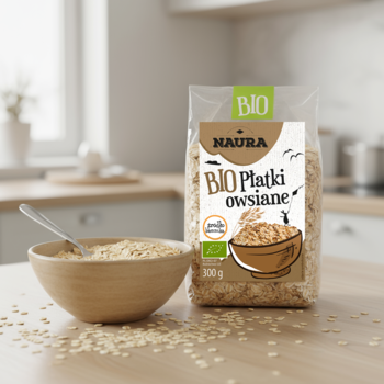 Bio płatki owsiane Naura 300g w przezroczystej torebce obok drewnianej miski z płatkami na kuchennym blacie.