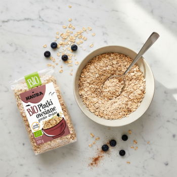 BIO płatki owsiane górskie drobne w torebce i misce, z jagodami na marmurowym tle, widok z góry.