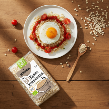 Opakowanie BIO kaszy jęczmiennej Madra na drewnianym stole, obok gotowe danie z kaszy, jajka i świeżych pomidorów.