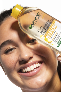 Uśmiechnięta kobieta z butelką płynu micelarnego Garnier z Witaminą Cg, rozświetla i oczyszcza skórę.