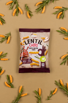 Opakowanie chipsów soczewicowych o smaku klonowego boczku, otoczone rozsypanymi chipsami i gałązkami. Widok z góry.