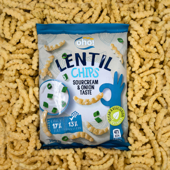 Paczka Ohoi Lentil Chips śmietankowo-cebulowych, otoczona pofalowanymi chipsami z czerwonej soczewicy. Widok z góry.