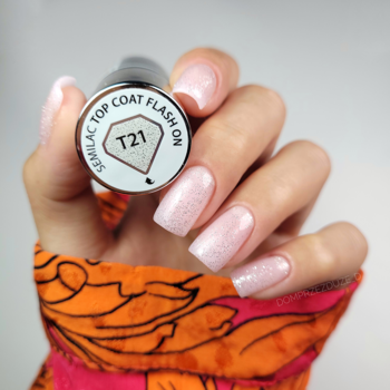 Zbliżenie na dłoń z błyszczącymi, brokatowymi paznokciami, trzymającą butelkę Semilac Top Coat Flash On T21.
