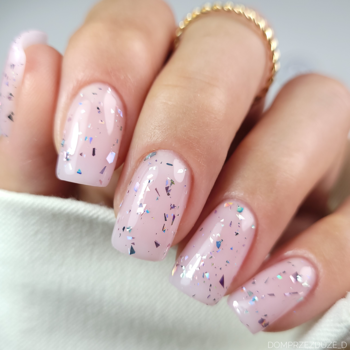 Zbliżenie na dłoń z paznokciami, Top Flower Flakes: bezbarwny top z liliowo-różowymi i szmaragdowo-srebrnymi płatkami holo.