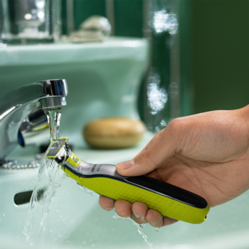 Męska golarka Philips OneBlade (zielono-czarna) płukana pod bieżącą wodą z kranu w łazience.