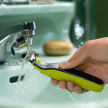 Philips OneBlade, wodoodporna golarka do włosów, trzymana pod bieżącą wodą w jasnym, zielonym zlewie.