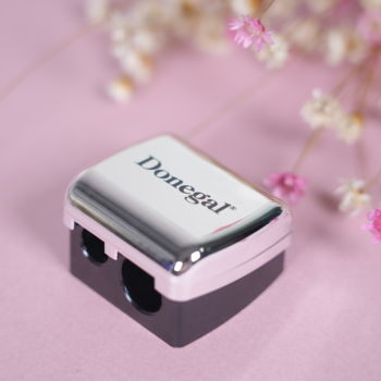 Metaliczna temperówka kosmetyczna Donegal do kredek i ołówków, srebrno-czarna, na różowym tle z kwiatami.